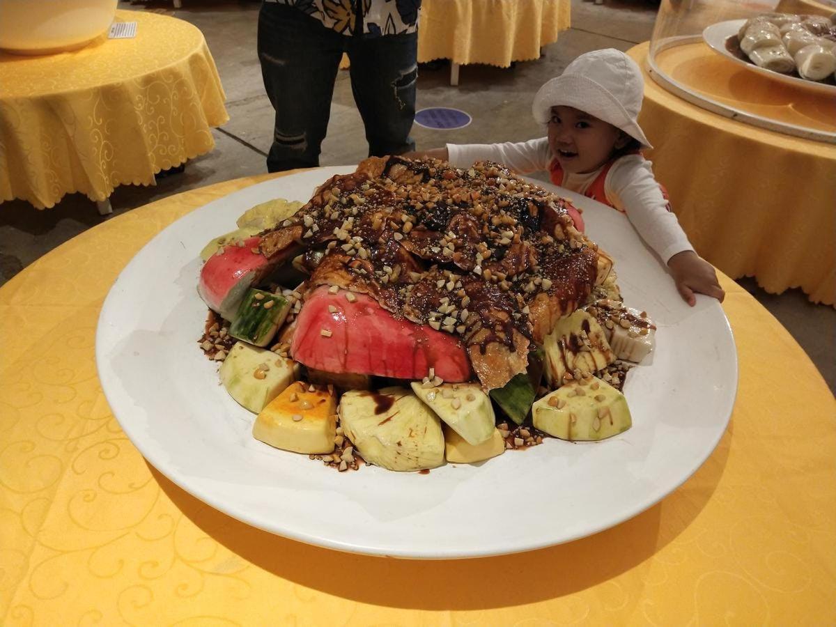 a little girl standing in front of a plate of food