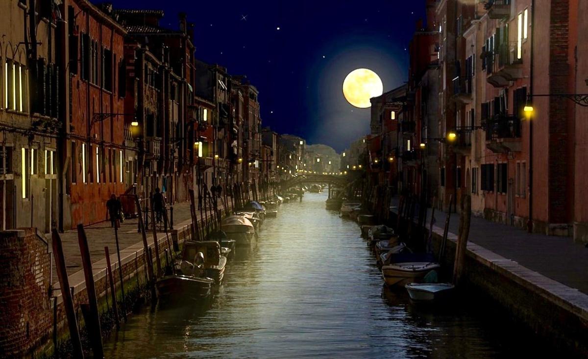 a canal in a city at night with a full moon