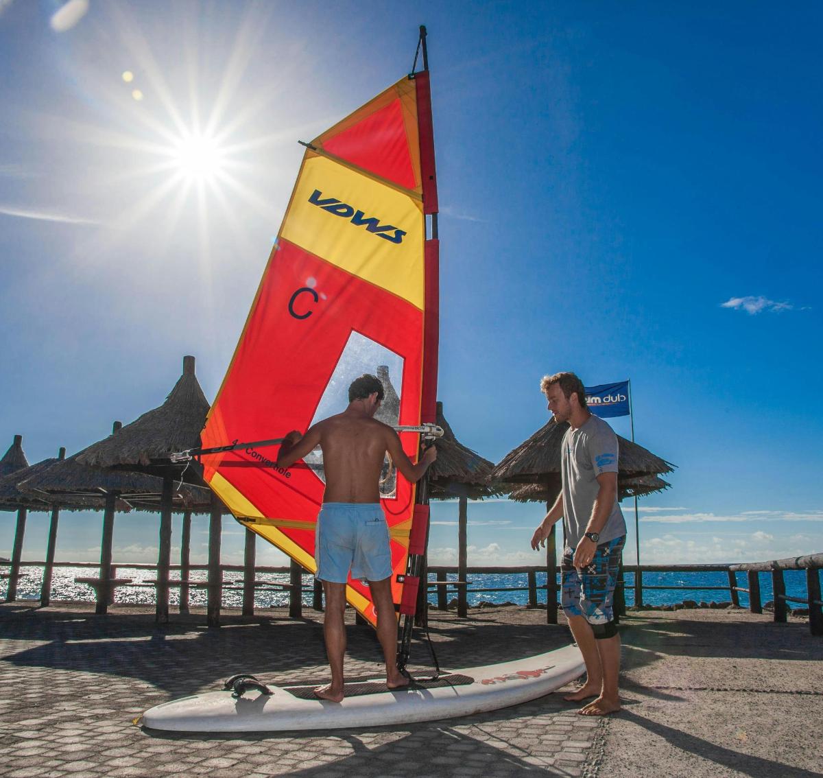 Dos hombres de pie sobre una tabla de surf con una vela