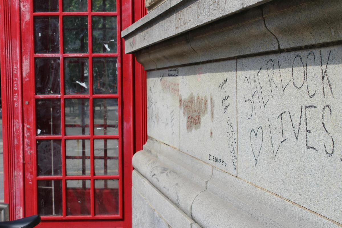 a wall with graffiti on it with two red phone booths