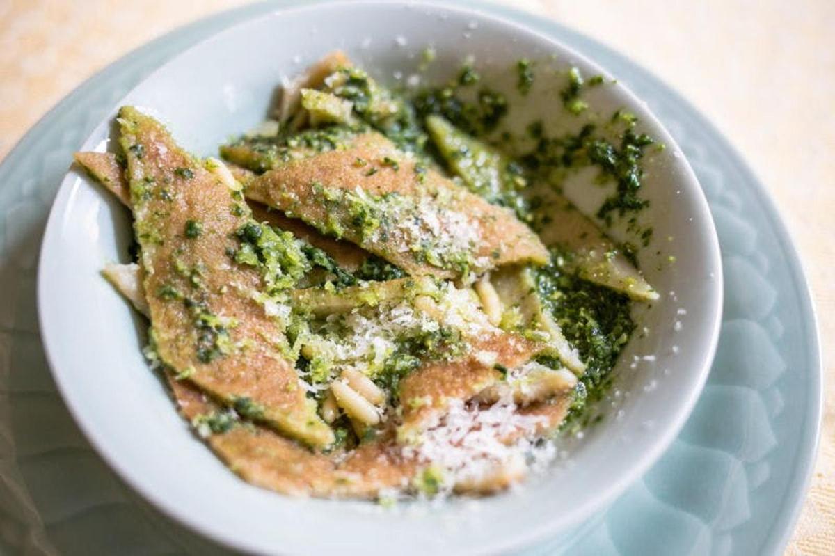 a white bowl of food with pesto and pasta