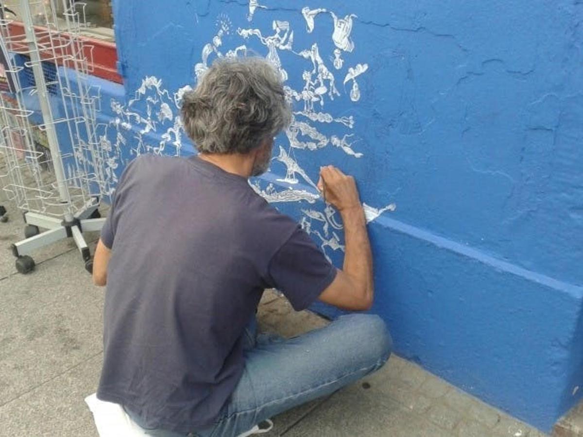 Un hombre sentado en el suelo pintando una pared azul.