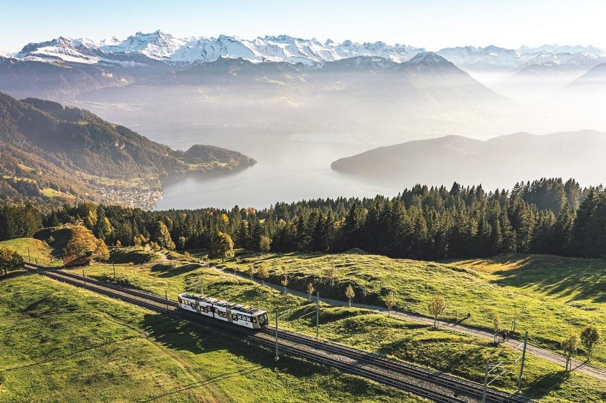 um trem viajando por um vale com um lago e montanhas