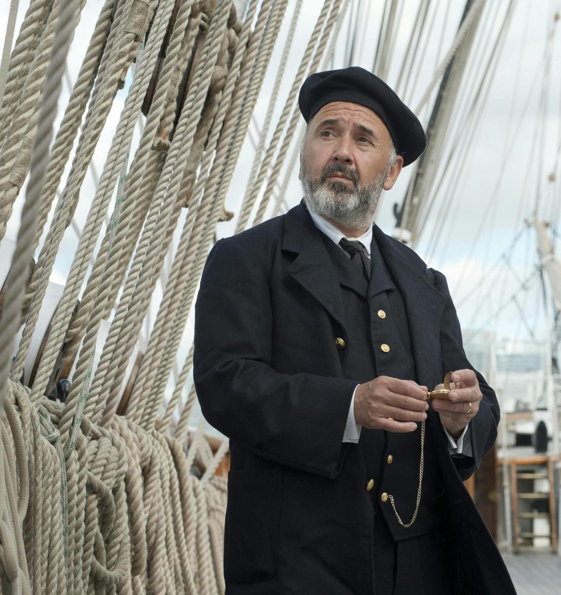 a man in a suit and hat standing next to a ship