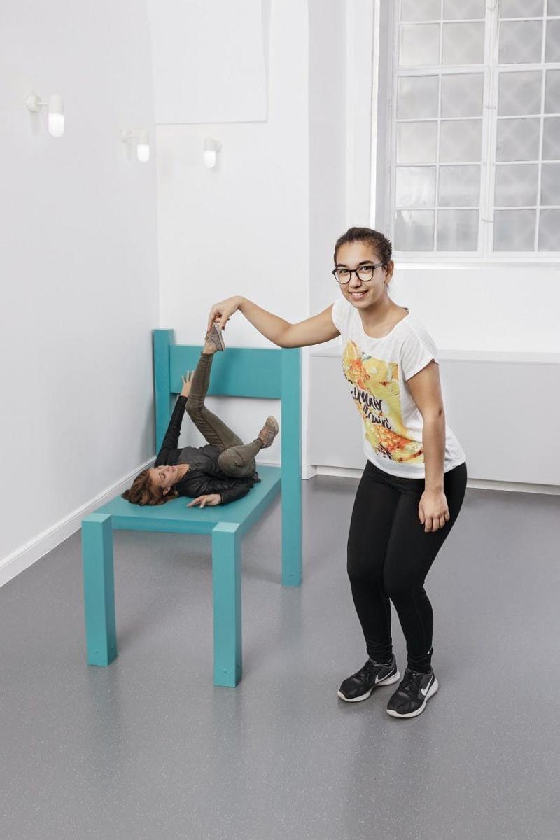 Una mujer parada junto a una silla azul con una persona.
