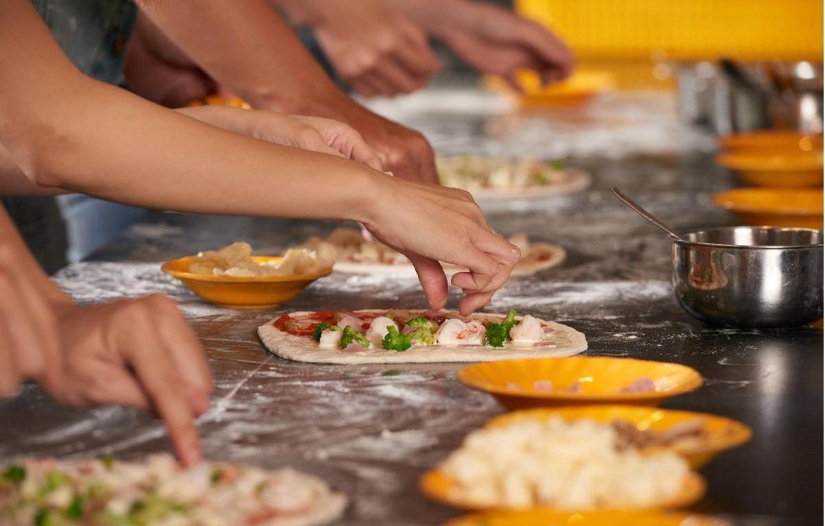 a group of people making pizzas in a kitchen