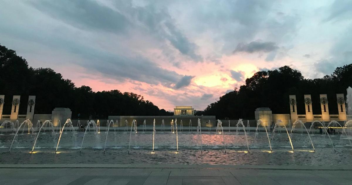 Una fuente con un edificio al fondo con una puesta de sol.