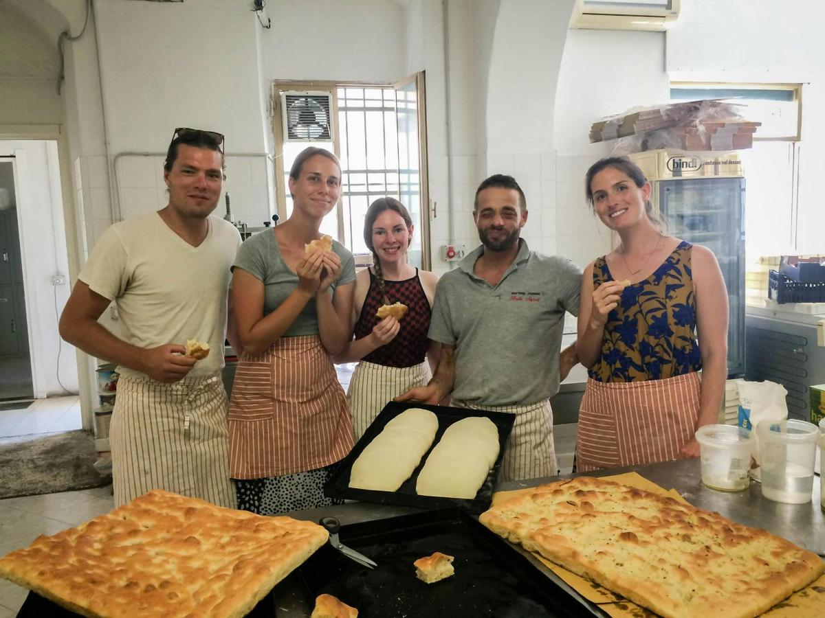 skupina lidí stojících v kuchyni s pizzou