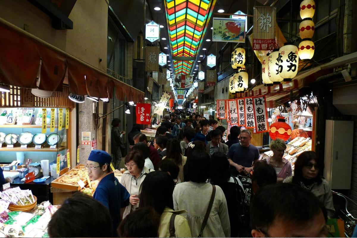 a crowd of people walking through a food market
