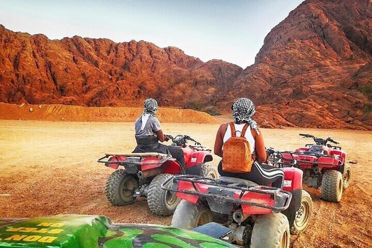 Două persoane stau pe ATV-uri în deșert