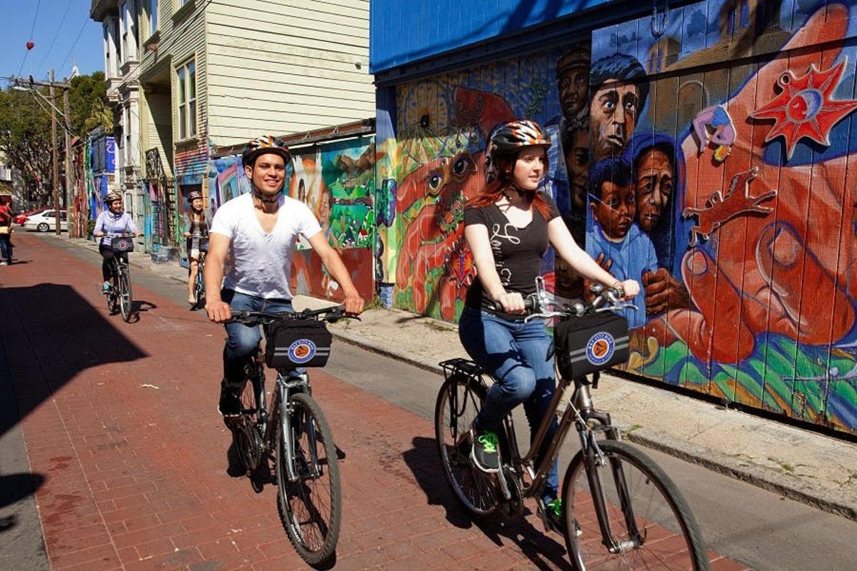 un home i una dona anant en bicicleta per un carrer amb grafits