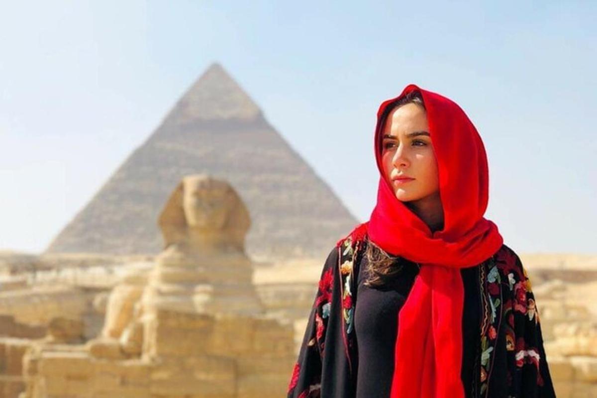 una dona amb un hijab vermell dempeus davant de les piràmides