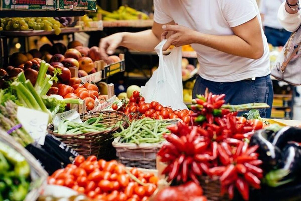 seseorang yang memegang beg tomato dan sayur-sayuran di pasar