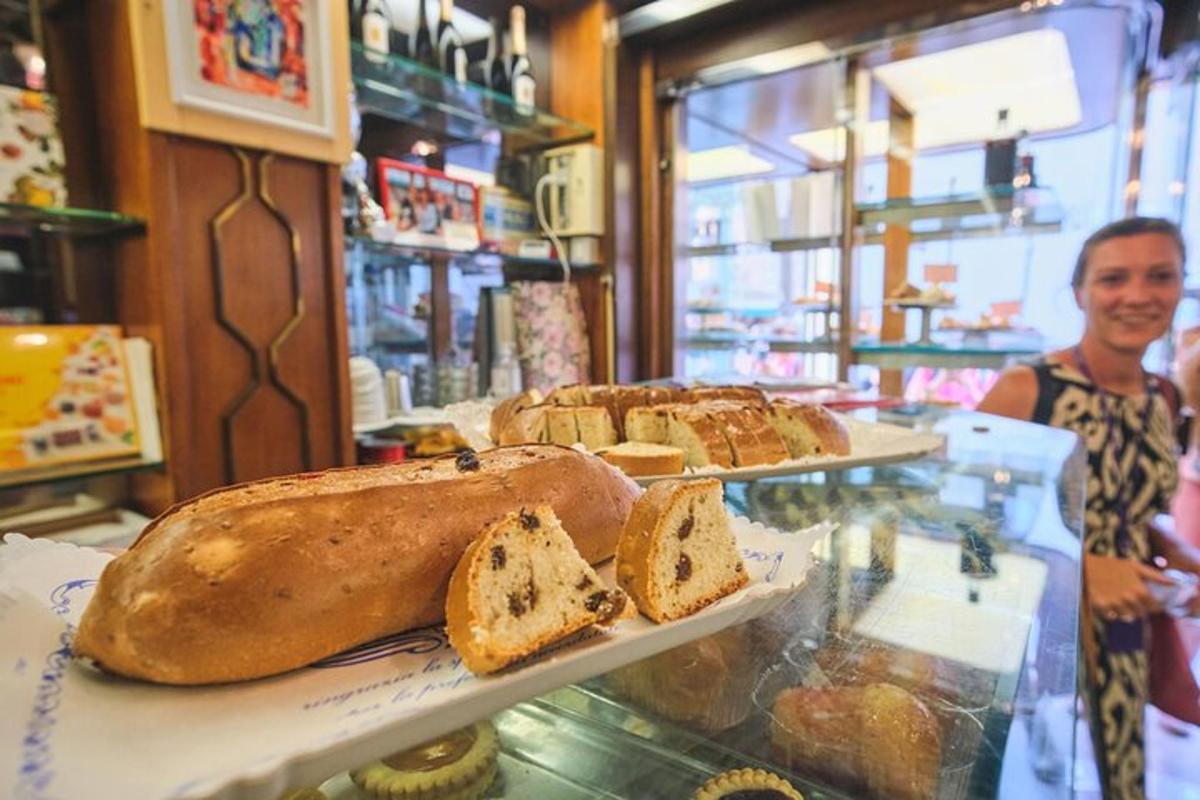 um homem parado em uma padaria com três bandejas de pão