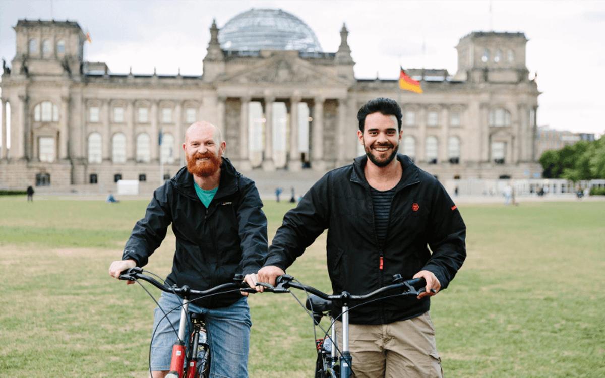 two men holding their bikes in front of a building