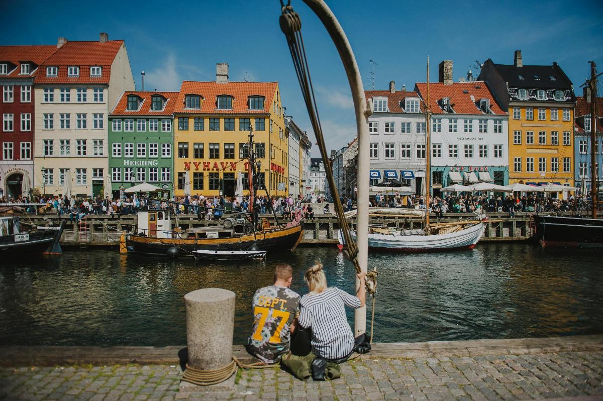 two people sitting on a dock near a river with boats