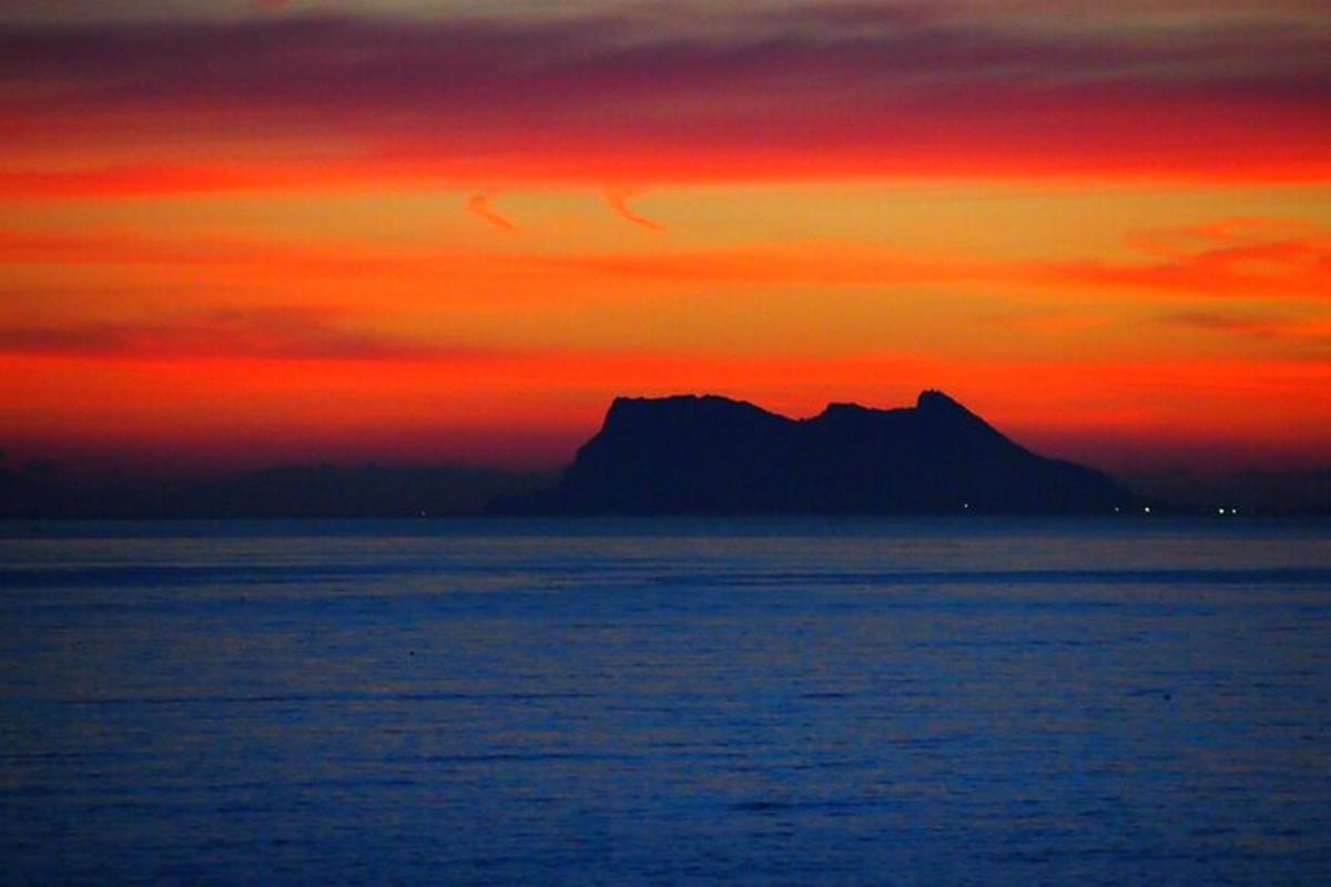 sončni zahod nad oceanom z goro v ozadju