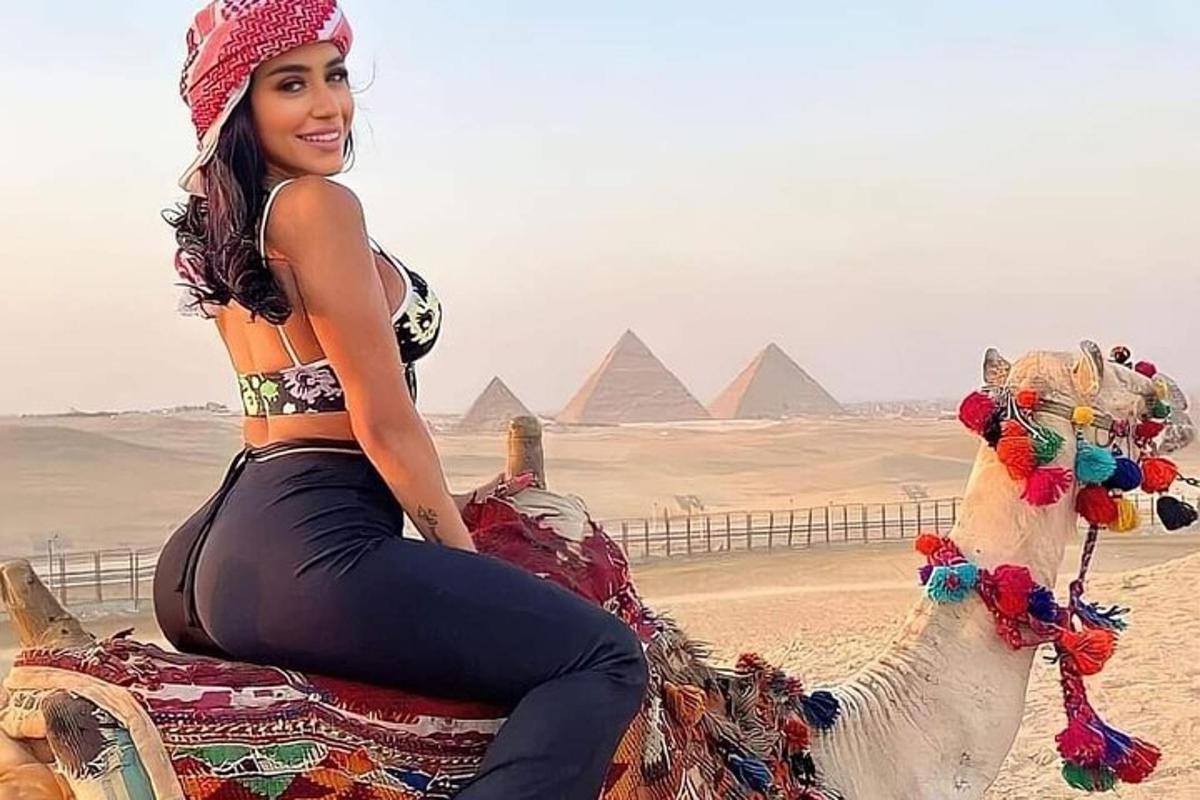 אישה יושבת על גמל מול הפירמידות