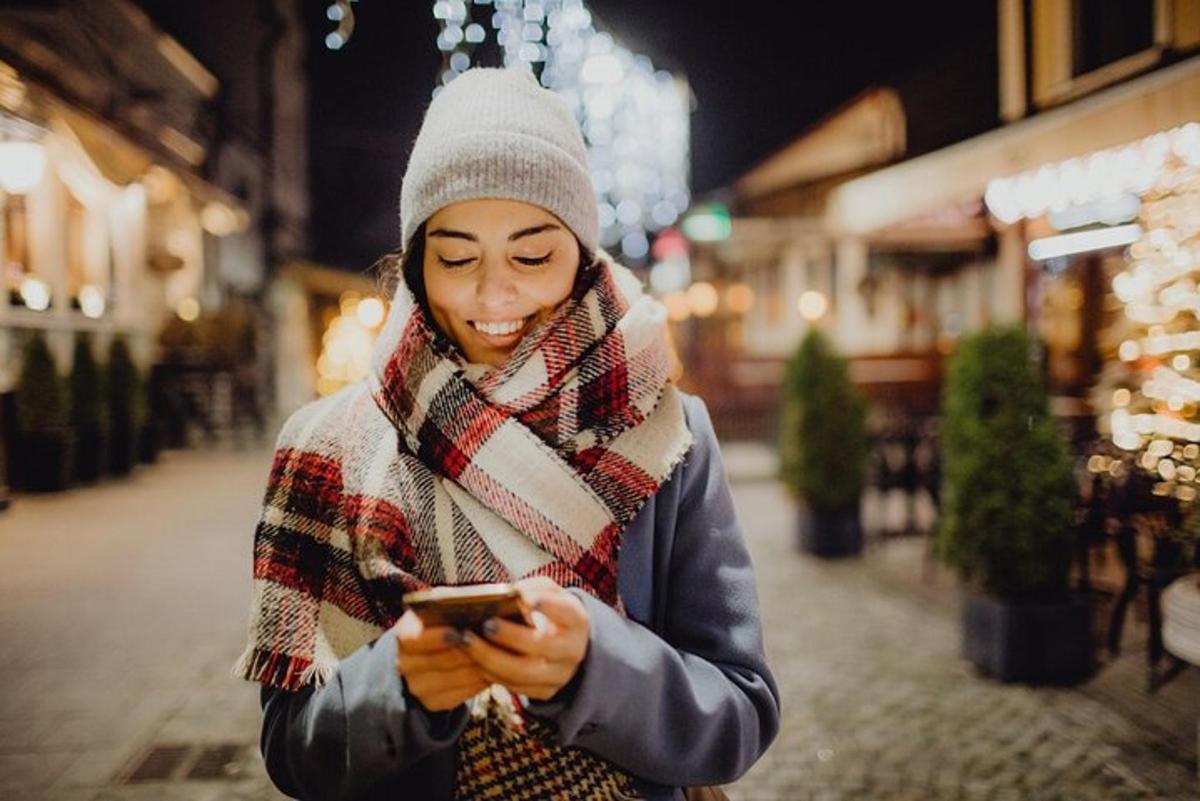 egy sálat viselő nő a mobiltelefonját nézi