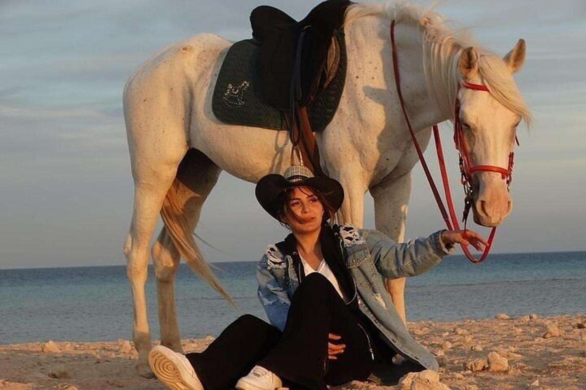 een vrouw zittend op het strand naast een wit paard