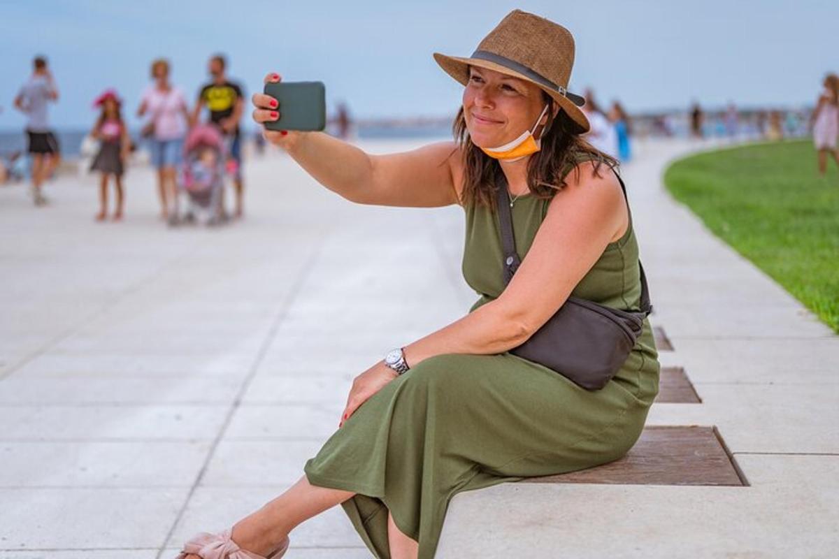 žena sedící na chodníku a fotící si mobilním telefonem