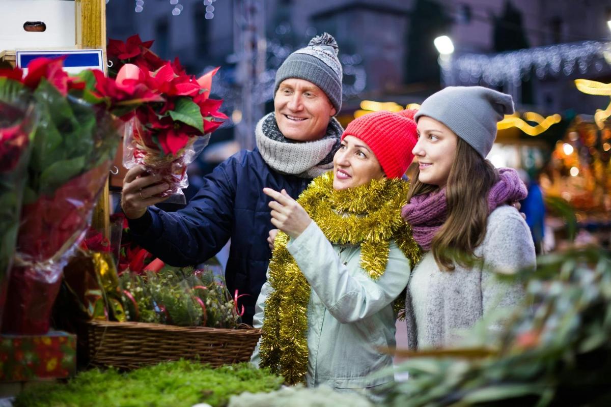 Un hombre y dos mujeres mirando flores en un mercado.