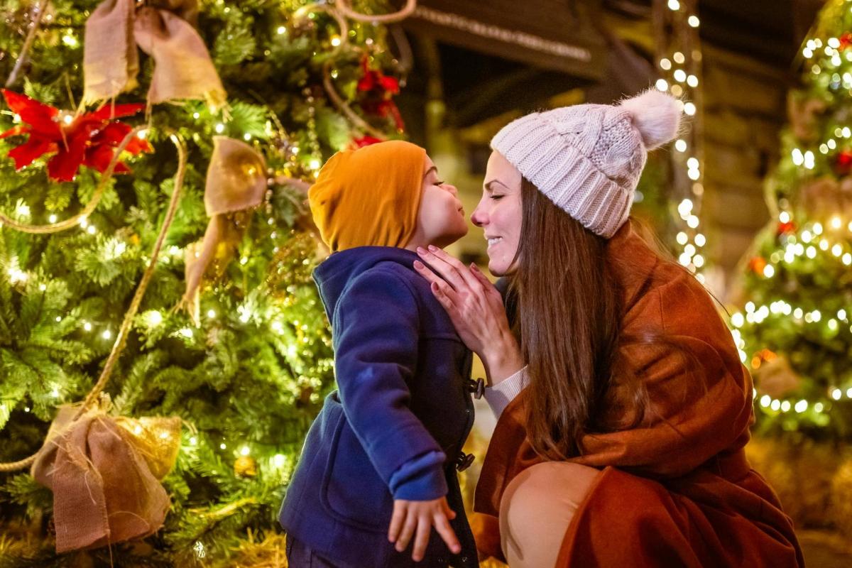 Una mujer y un niño de pie junto a un árbol de Navidad.