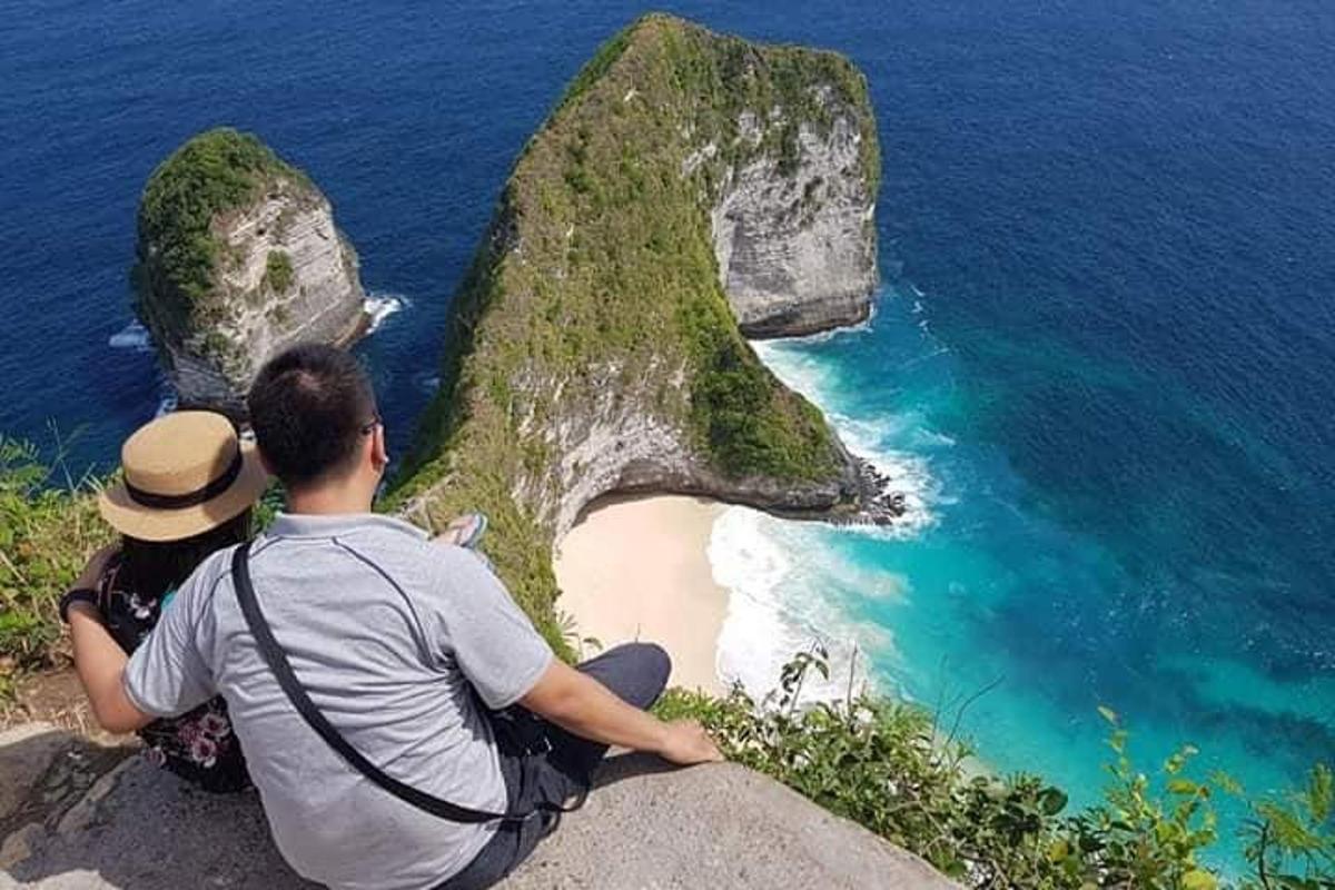 two people sitting on a rock looking at the ocean
