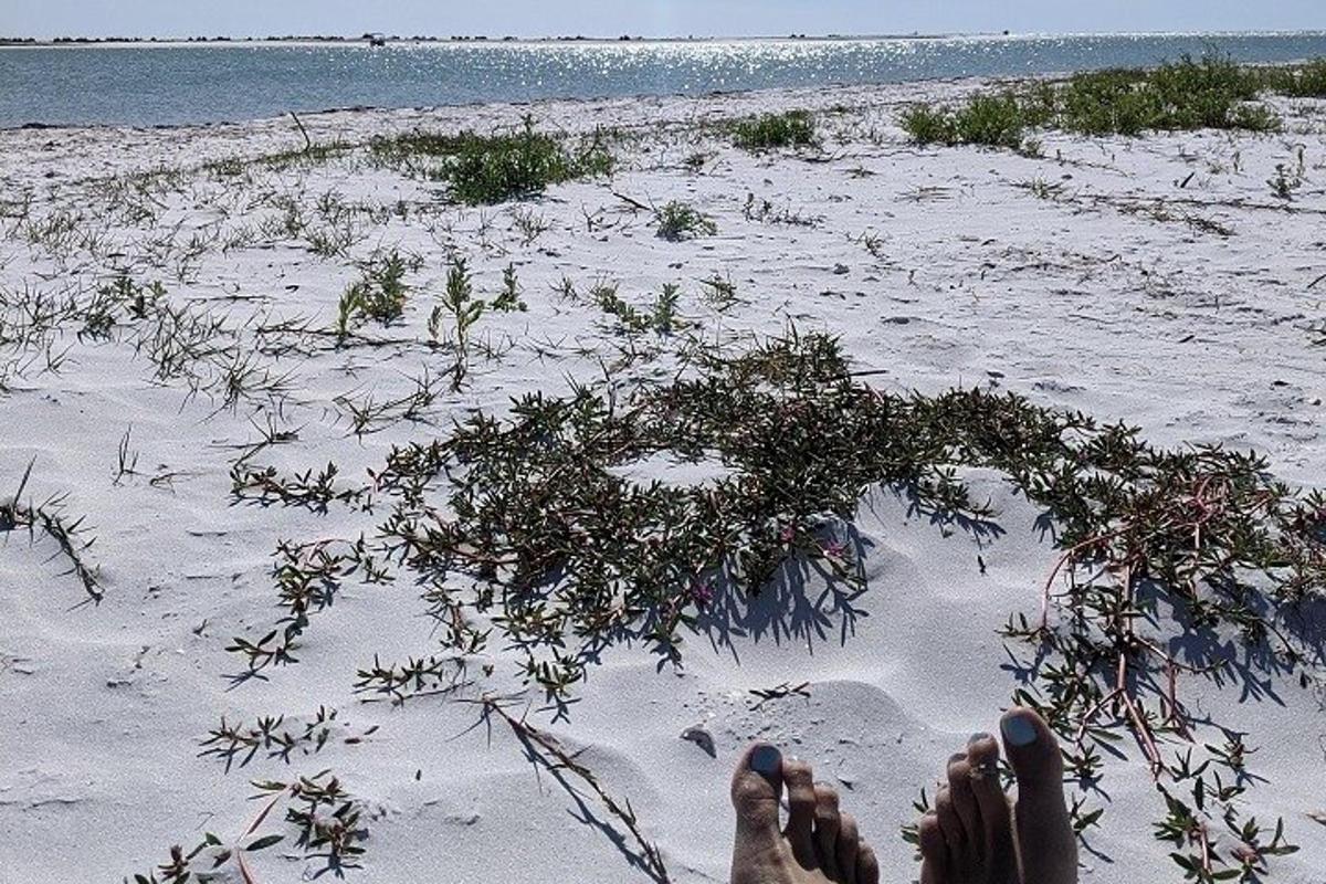 seseorang berbaring di pantai dengan kaki mereka di dalam pasir