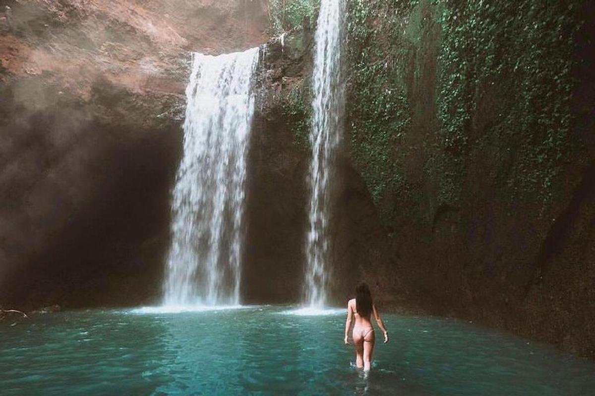Una mujer parada en el agua frente a una cascada.