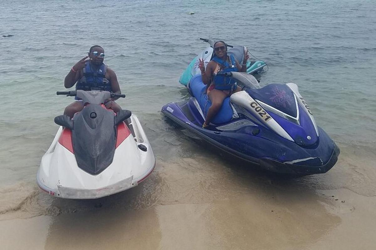 Două persoane se plimbă cu un jet ski pe plajă