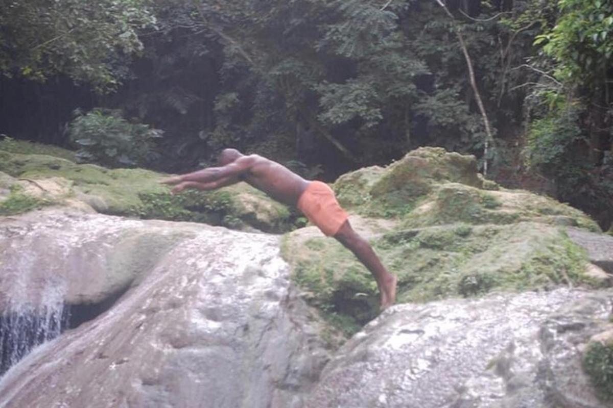 Un hombre haciendo una parada de manos sobre una roca cerca de una cascada.