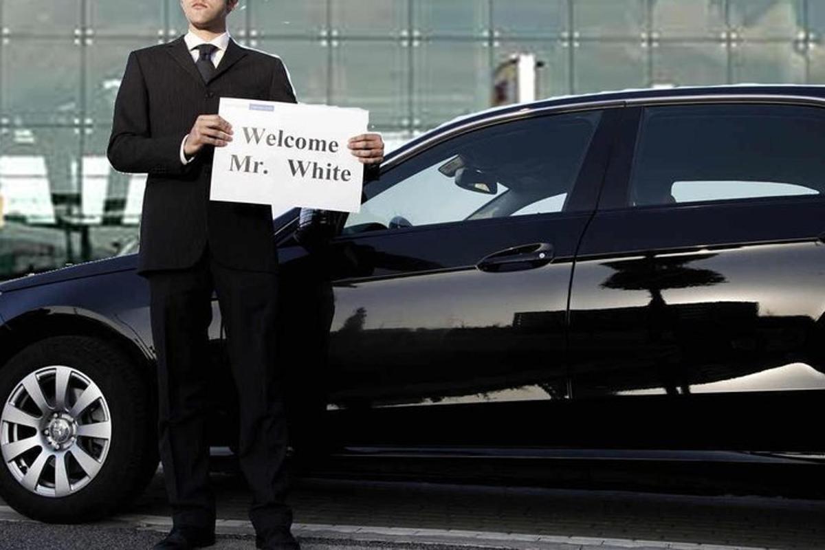 um homem de terno segurando uma placa na frente de um carro