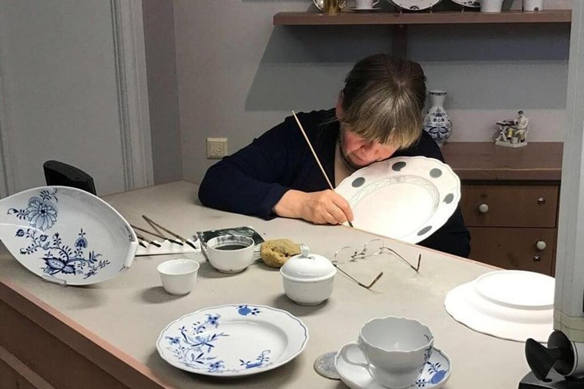Un hombre dibujando sobre una mesa con platos azules y blancos.