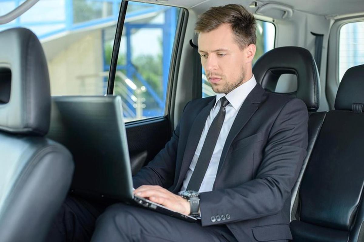 um homem de terno e gravata sentado em um carro usando um laptop