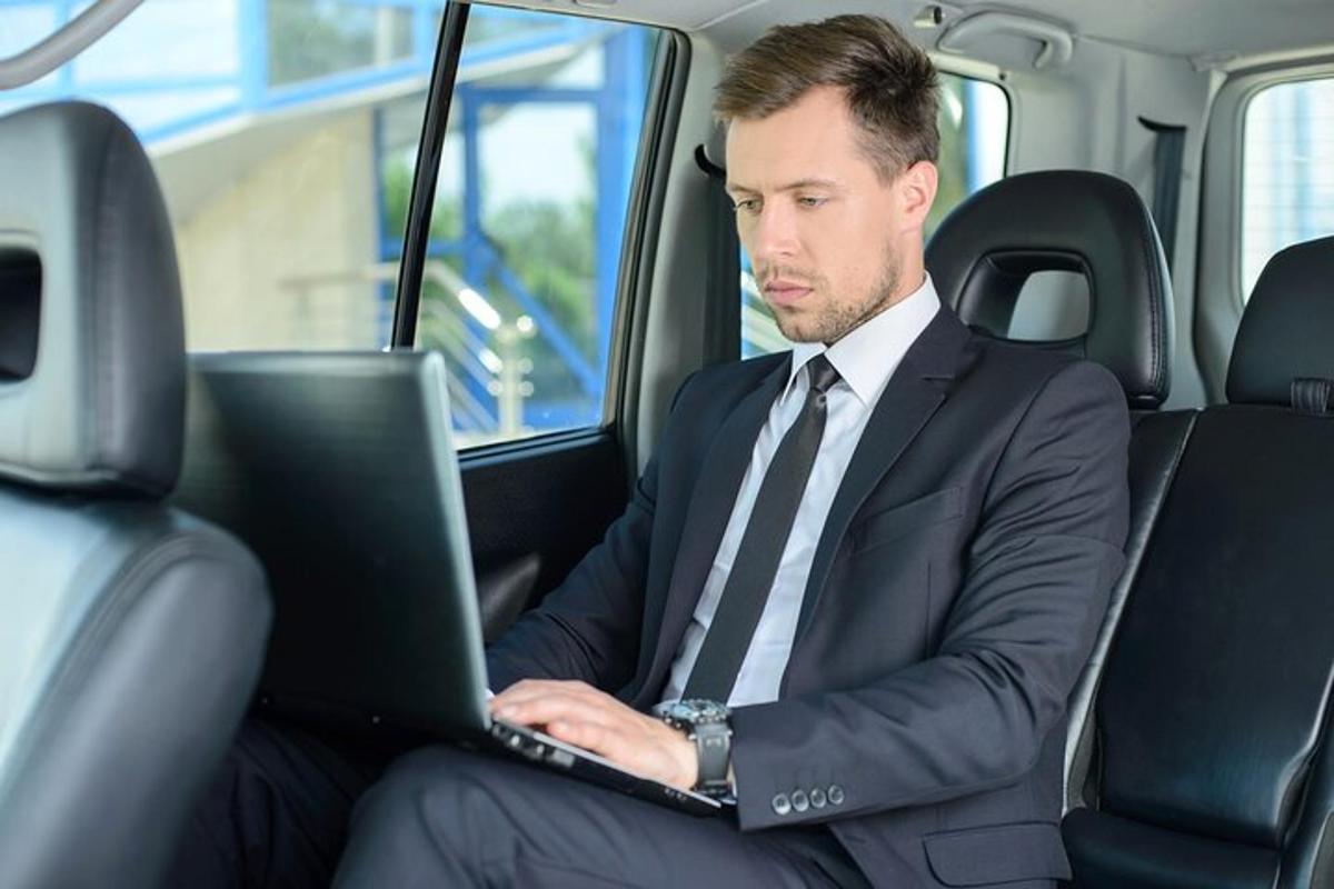 un uomo in giacca e cravatta seduto in macchina mentre usa un computer portatile