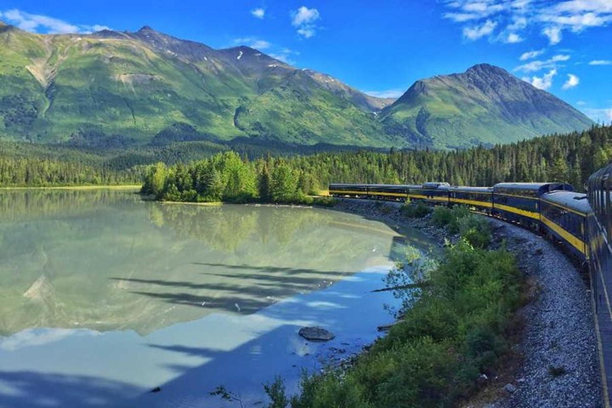 a train on a track near a river and mountains
