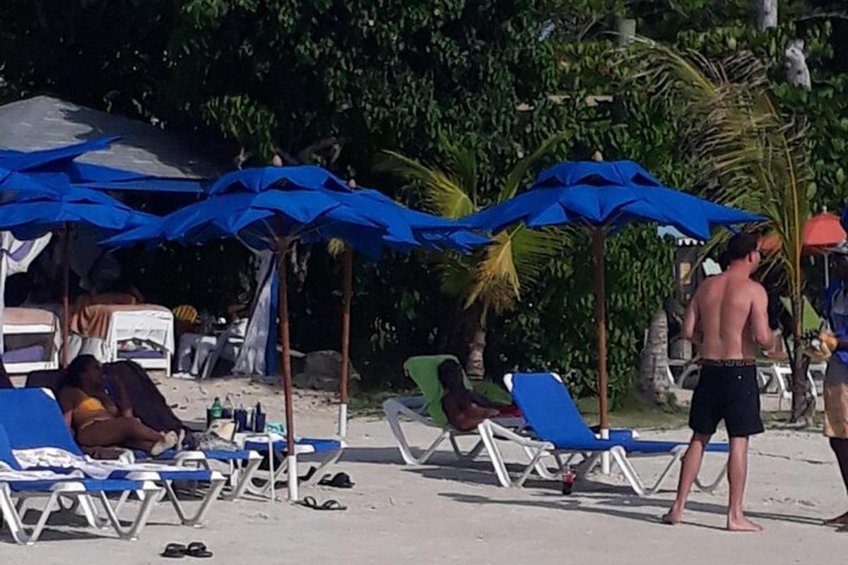 Skupina lidí sedících na pláži pod modrými slunečníky