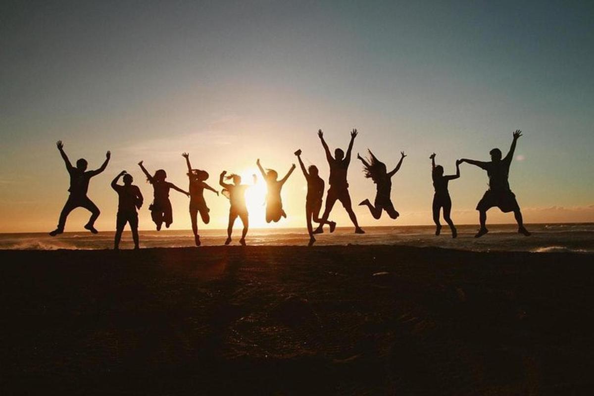 um grupo de pessoas pulando na praia ao pôr do sol