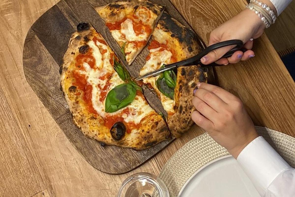 una persona tallant una pizza sobre una taula de fusta