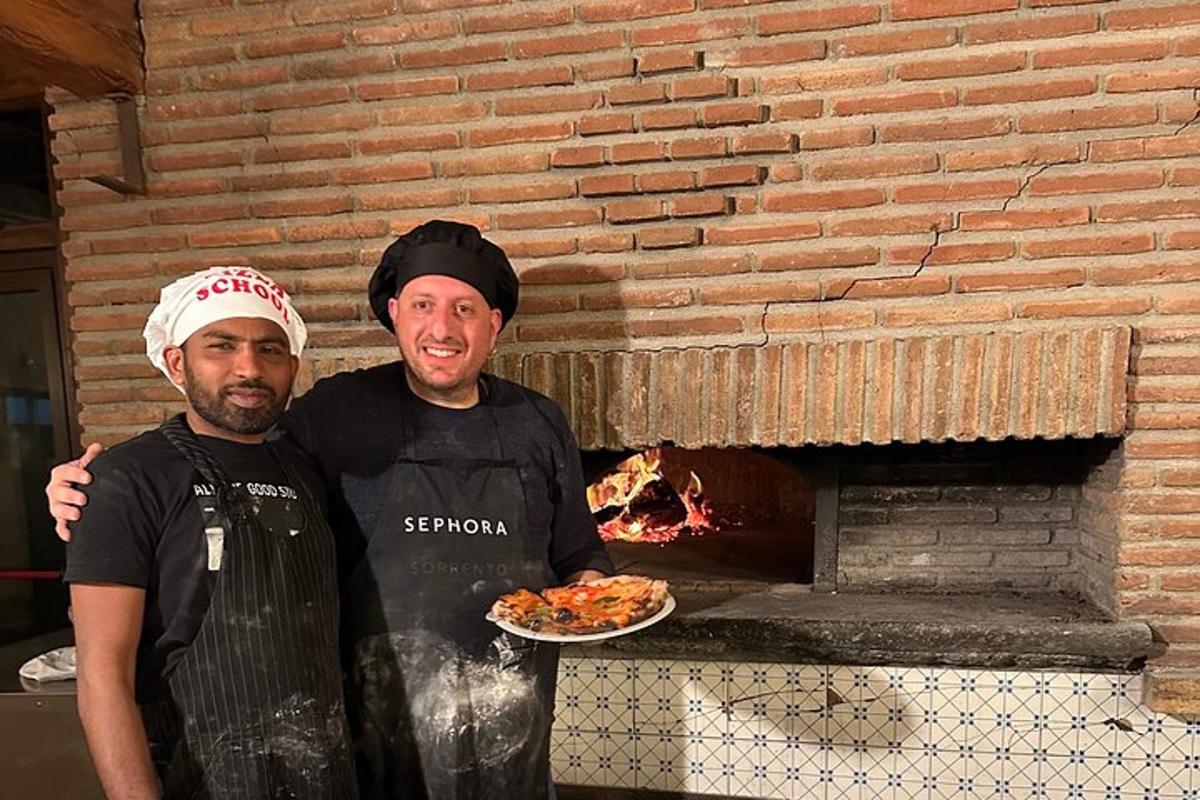 two men standing in front of a pizza oven