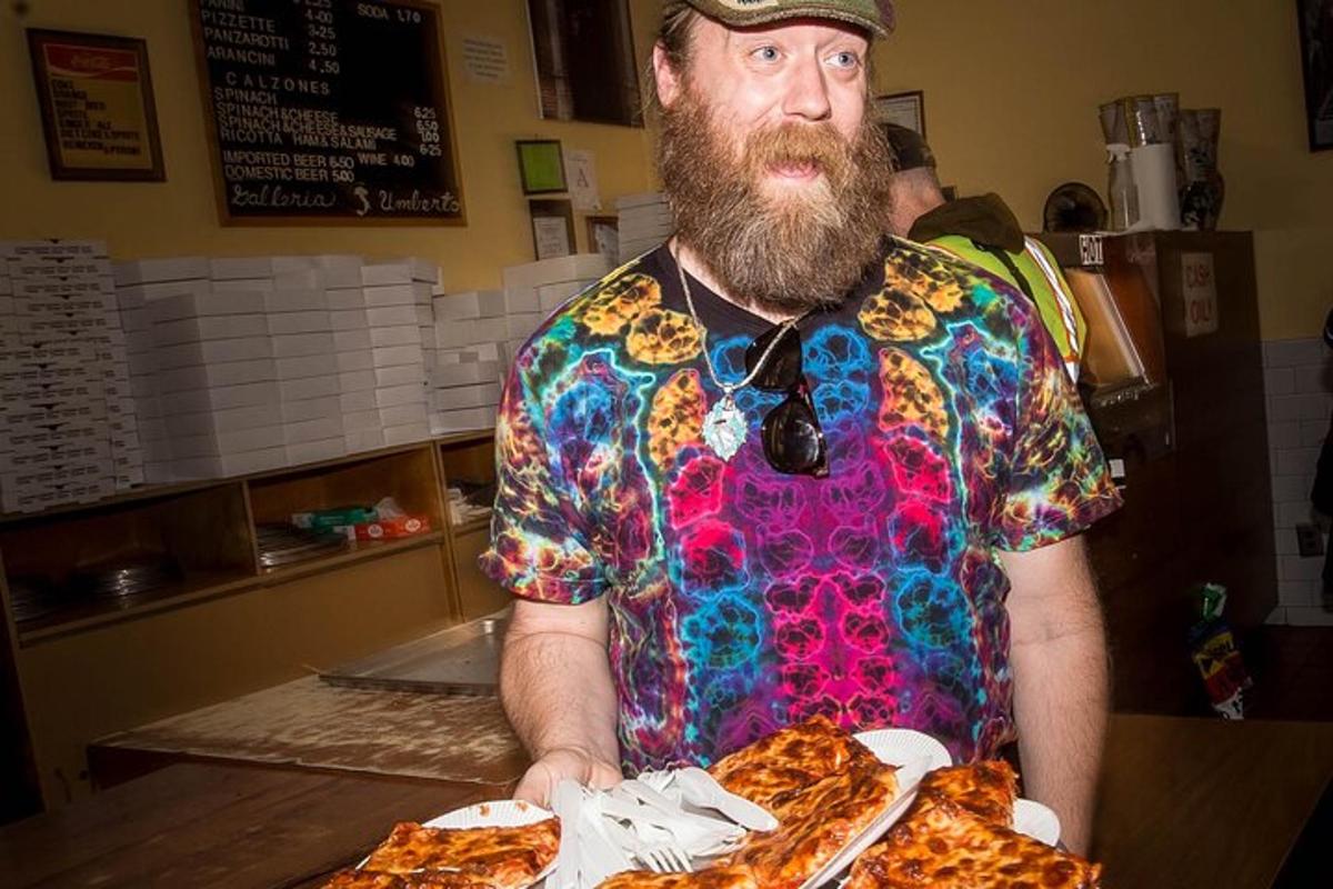 seorang pria berjanggut memegang sepiring pizza