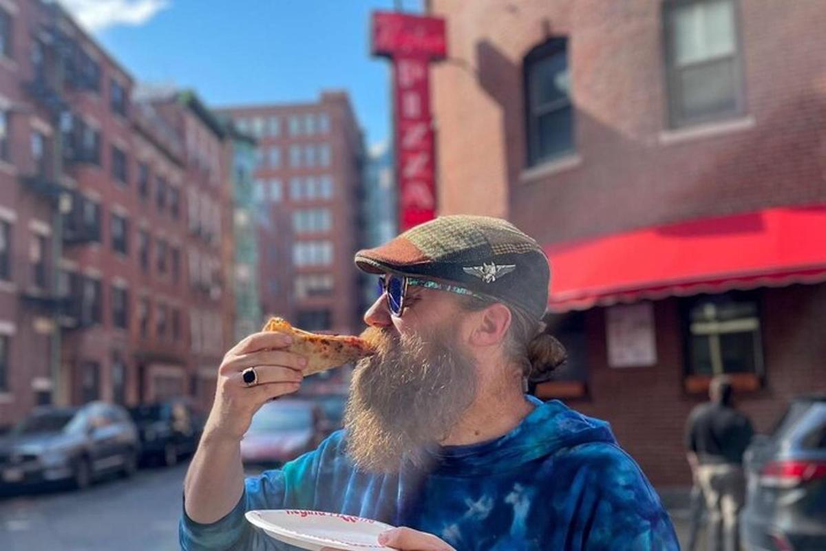 seorang pria berjanggut sedang makan sepotong pizza