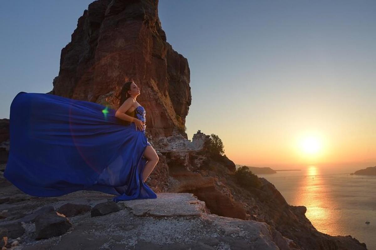 a woman in a blue dress sitting on a cliff at sunset