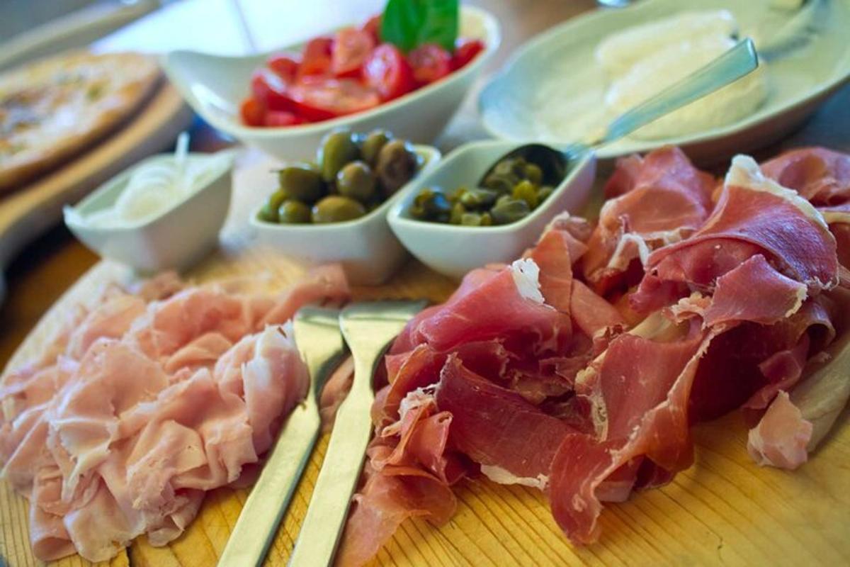 papan pemotong dengan ham dan makanan lain di atas meja
