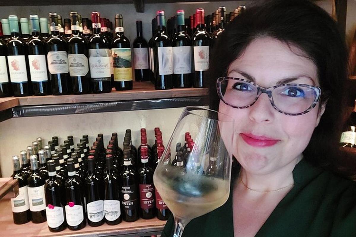 ženska, ki drži kozarec vina pred steklenicami vina