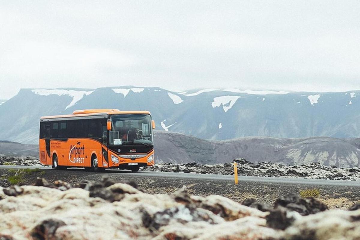 an orange bus driving down a road with mountains in the background