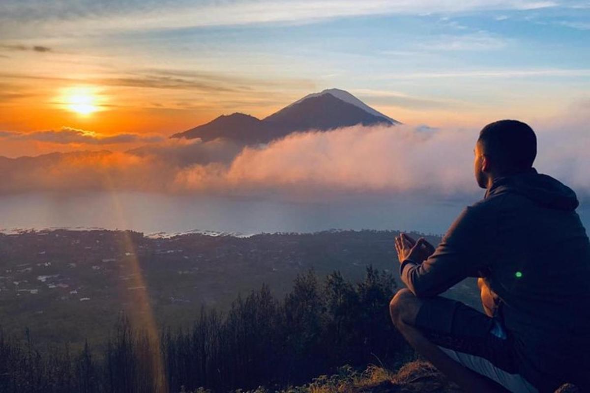 seorang pria duduk di puncak gunung saat matahari terbenam