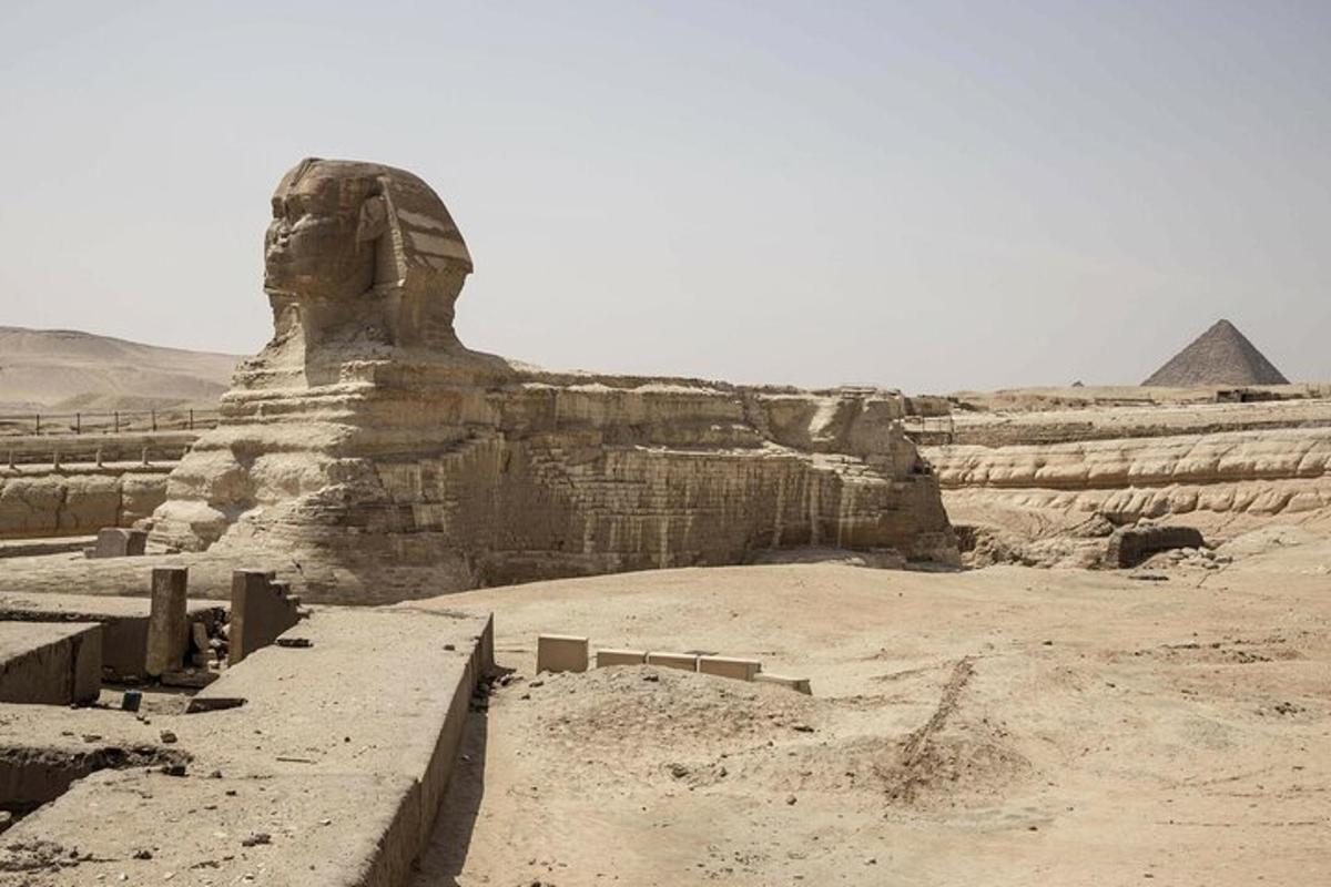 a statue in the desert with the pyramids in the background