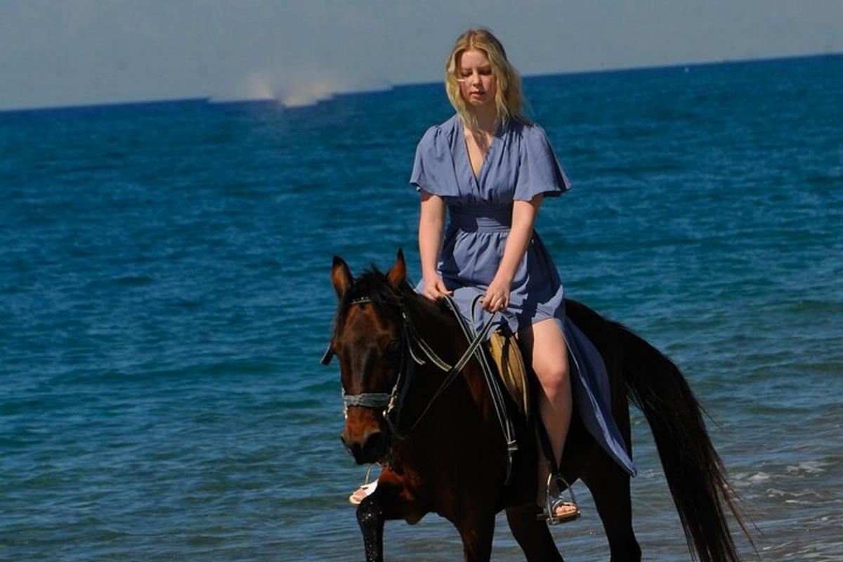 eine Frau in einem blauen Kleid, die auf einem Pferd am Strand reitet